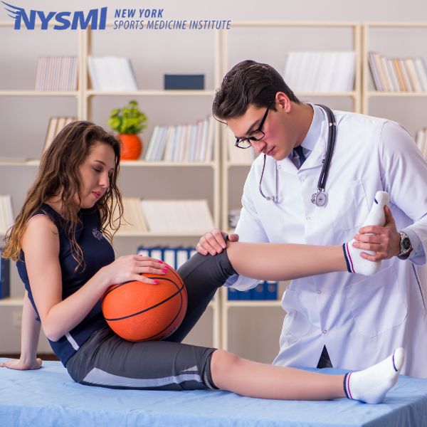 A doctor examines a female basketball player's leg while she holds a basketball, in a medical office. NYSMI logo appears in the top left corner.